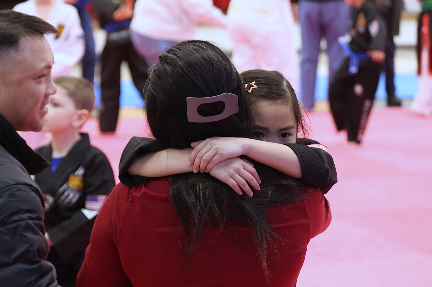 A mother in dobok hugged by her daughter at Bill Cho's, father smiling in foreground